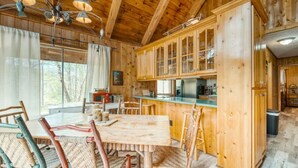 Interior rústico de una cabaña de madera con comedor, cocina y ventanas amplias.