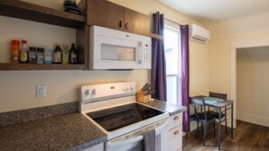 A compact kitchen with a stove, microwave, and a small dining area with a table and chairs. - Downtown Studio w/Huge Balcony ·King Bed ·Walkable (Eugene)