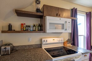 Una cocina con microondas, estufa y diversos utensilios de cocina en estantes.