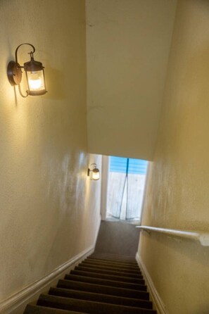 A staircase with a handrail, light fixtures on the walls, and a view of the outside.