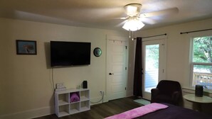 A room with a bed, a TV, a door, a chair, and a window. - Downtown Studio w/Huge Balcony ·King Bed ·Walkable (Eugene)
