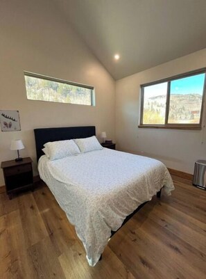 Ein Schlafzimmer mit einem großen Bett, zwei Nachttischen, einem Fenster mit Blick auf die Berge und einer Deckenleuchte.