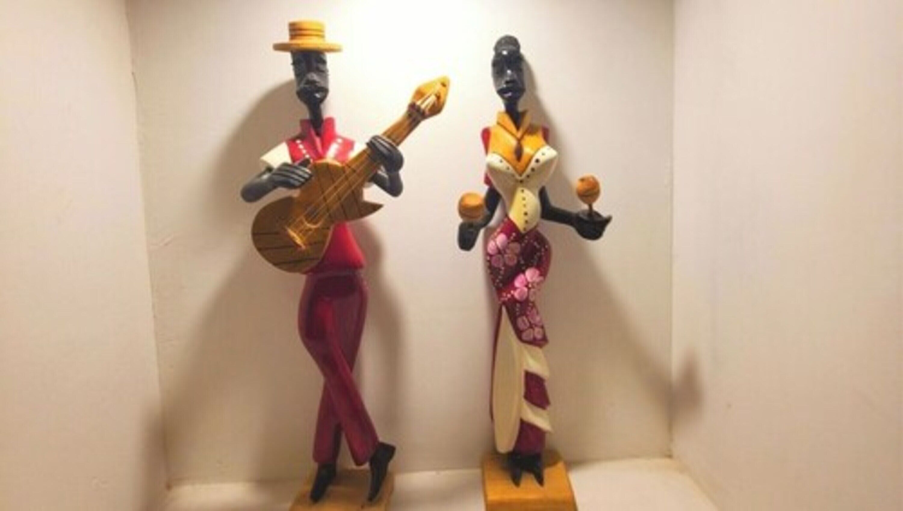 Twee houten sculpturen van figuren, waarvan één een gitaar vasthoudt en de andere maracas.