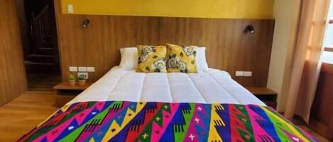 A hotel room with a large bed, wooden headboard, and a colorful bedspread.