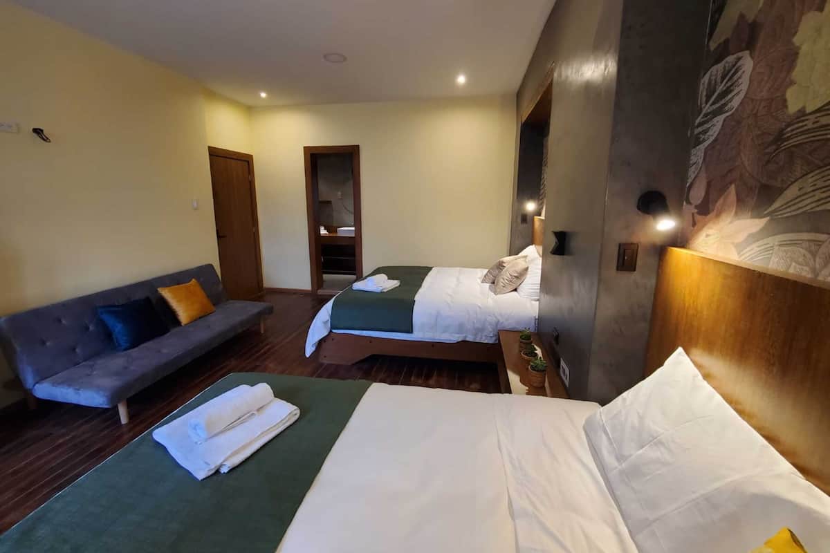 A hotel room with two beds, a sofa, and a small table with a plant.