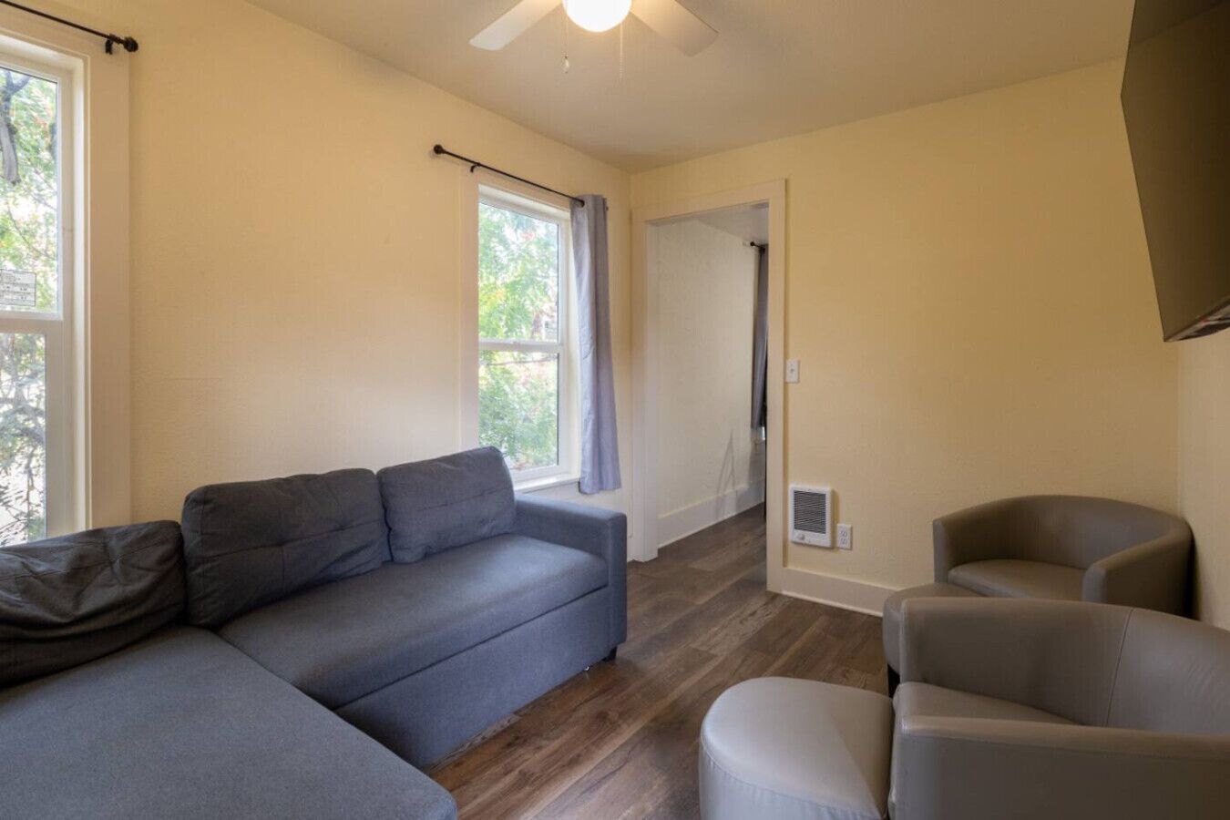 A living room with a sofa, armchairs, a ceiling fan, and a door leading to another room.