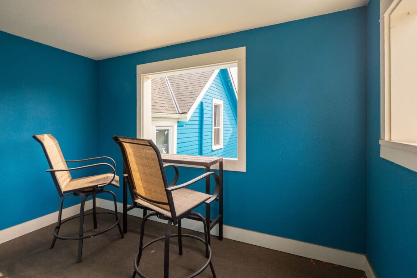 A room with two chairs, a window, and a view of a house.