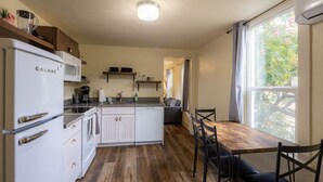 Een kleine keuken met een koelkast, magnetron en een houten eettafel met stoelen.