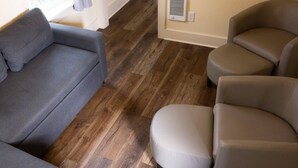 Een woonkamer met een grijze bank, beige fauteuils en een houten vloer.