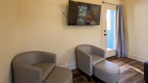 Een kamer met twee fauteuils, een flatscreen televisie aan de muur, een deur met gordijn en houten vloer.