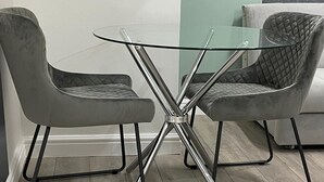 A modern dining area with a glass table and two upholstered chairs.