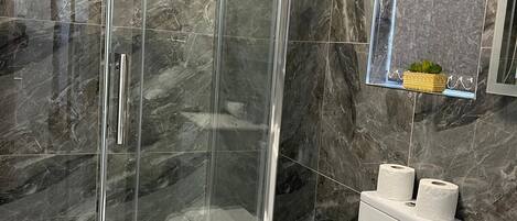 A modern bathroom with a glass-enclosed shower, marble walls, a toilet, and a sink.