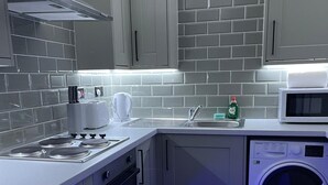 A compact kitchen with grey cabinets, a built-in microwave, a washing machine, and a toaster.