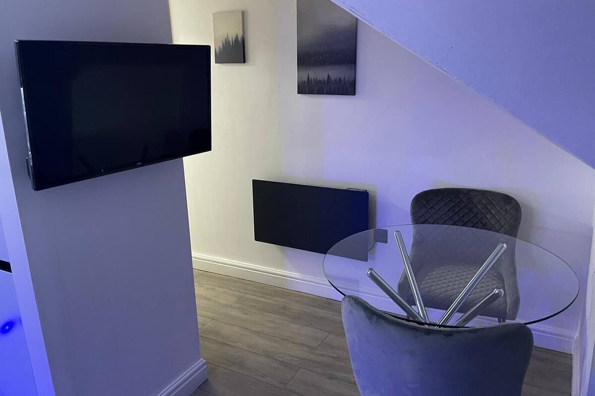 A modern living room with a flat-screen TV mounted on the wall, a glass coffee table, and a comfortable chair.