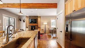 Eine moderne Küche mit Granitarbeitsplatten, einem Edelstahlkühlschrank, Holzausbau und einem Kamin aus Naturstein. Es gibt eine Essecke mit einem roten Teppich.