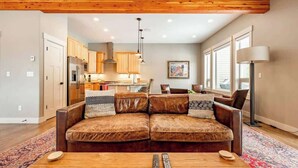 Ein Wohnzimmer mit braunem Ledersofa, einem Holztisch und einer Küche im Hintergrund.