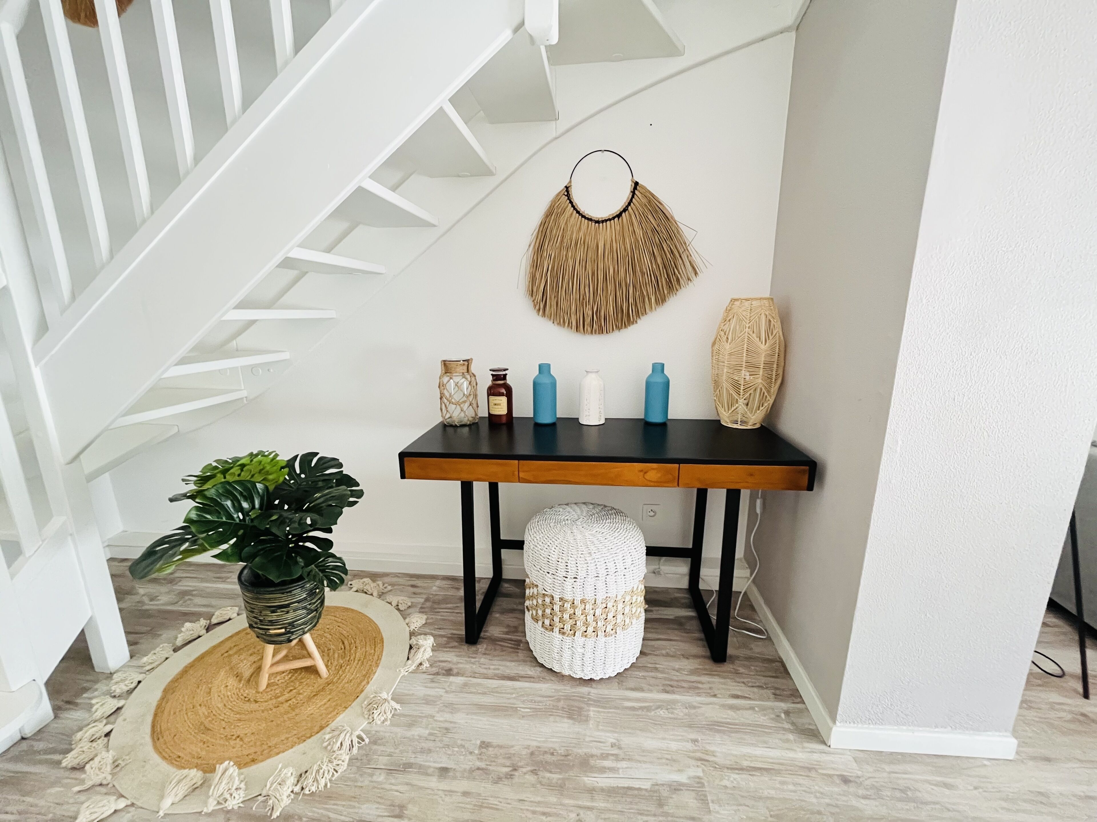 A staircase with white railings, a black table with decorative items, a woven basket, and a potted plant.