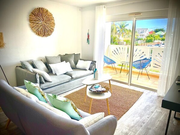 A living room with a grey sofa, a coffee table, and a view of the outside balcony.