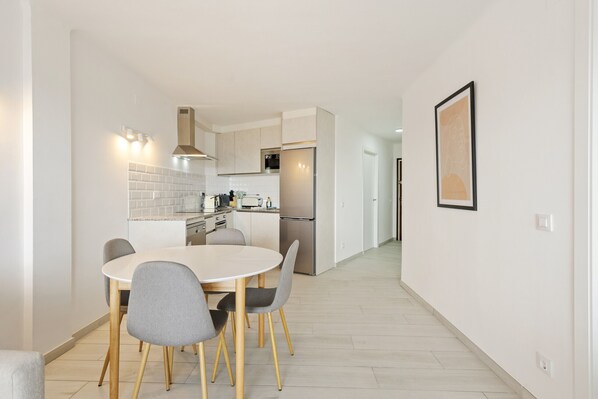 A modern kitchen with a dining area, featuring a white tiled backsplash, stainless steel appliances, and a light wood floor.