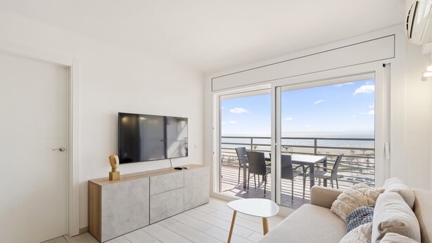 Una sala de estar moderna con televisor de pantalla plana, un sofá y un balcón con mobiliario exterior.