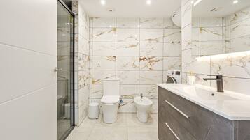 Een moderne badkamer met een glazen douchecabine, toilet, bidet en een wastafelmeubel met een wastafel en spiegel.