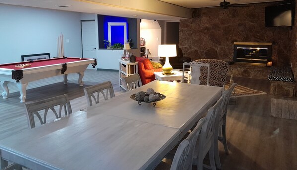 Un vaste salon comprenant une table de billard, un coin repas avec une table et des chaises, et un espace salon confortable avec un canapé et un fauteuil à motifs.