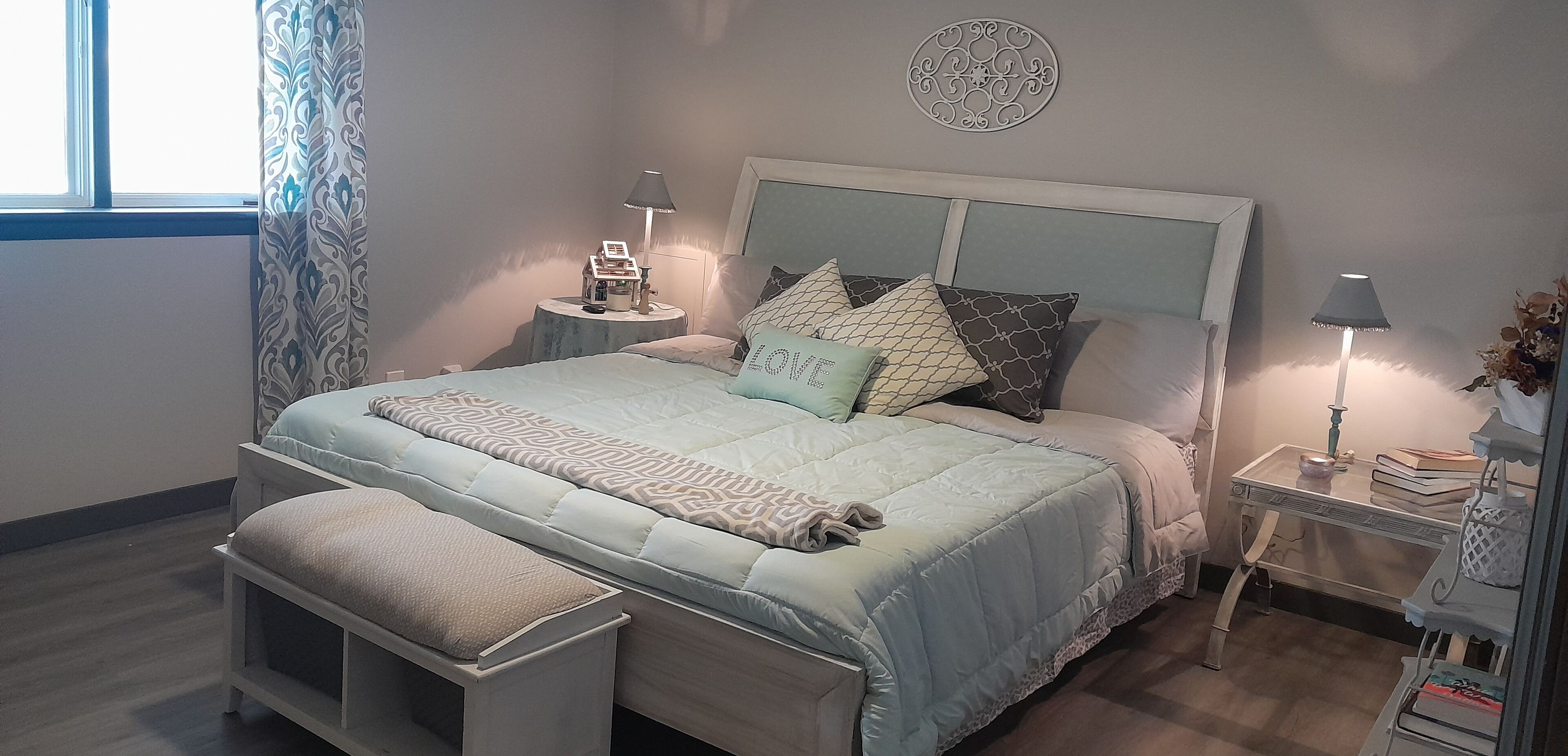 Una camera da letto ordinata con un letto, comodini, un tavolo da notte e una finestra con tende.