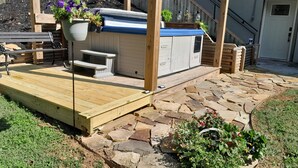 A wooden deck with a stone pathway leading to a small wooden structure with a blue roof, possibly a shed or storage unit. - Spacious, private retreat -  hot tub, firepit, pool table, dry sauna, patio (Oak Ridge)