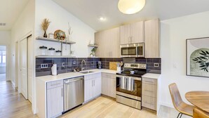 A modern kitchen with light wood cabinets, a stainless steel dishwasher, a microwave, and an oven. There is a dining area with a wooden table and chairs. - Beautiful Townhome - Steps to Downtown Boise! (Boise)