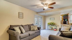 A living room with a grey sofa, a coffee table, and a ceiling fan. There are two framed signs on the wall and a door leading outside. - 1 Mi to MCAS New River: Peaceful Home w/ Patio (Jacksonville)