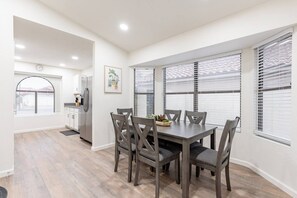 A modern kitchen with white cabinets, a stainless steel refrigerator, and a dining area with a wooden table and chairs.