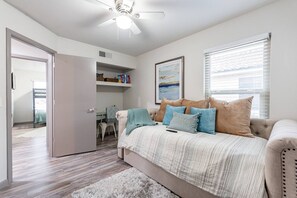 A bedroom with a bed, a ceiling fan, a window with blinds, and a door leading to another room.