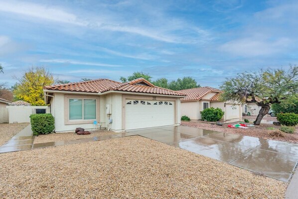A single-story house with a tiled roof, a garage, and a gravel driveway.