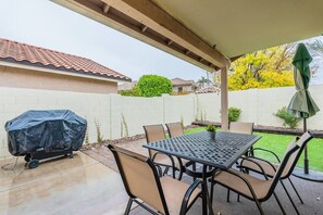 An outdoor patio with a covered table and chairs, a barbecue grill, and a green umbrella.