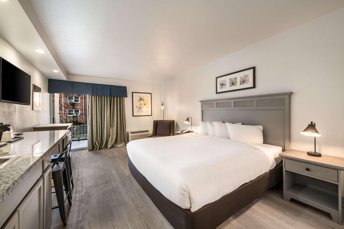 Habitación de hotel con cama, escritorio, silla, televisor y ventana con cortinas.