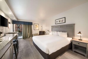 Habitación de hotel con cama, escritorio, silla, televisor y ventana con cortinas.