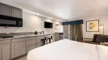 A hotel room with a bed, a kitchenette, a flat-screen TV, and a painting on the wall.