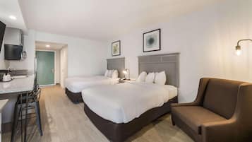 A hotel room with two beds, a sofa, a desk with a chair, and a TV mounted on the wall.