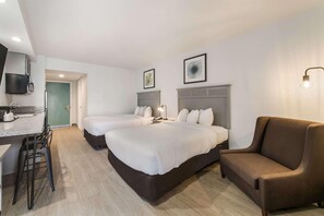 Quarto de hotel com duas camas, um sofá, uma escrivaninha com cadeira e uma televisão na parede.