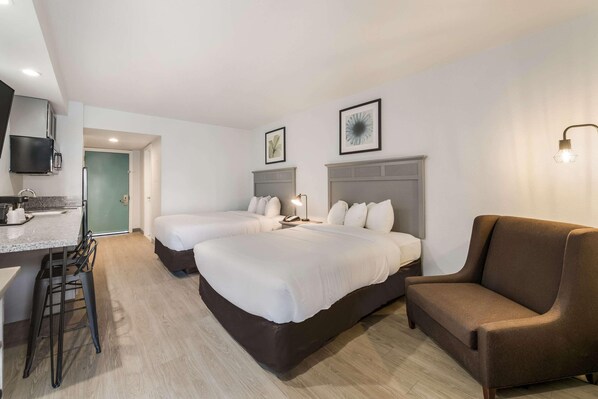 Habitación de hotel con dos camas, un sofá, un escritorio con silla y un televisor montado en la pared.