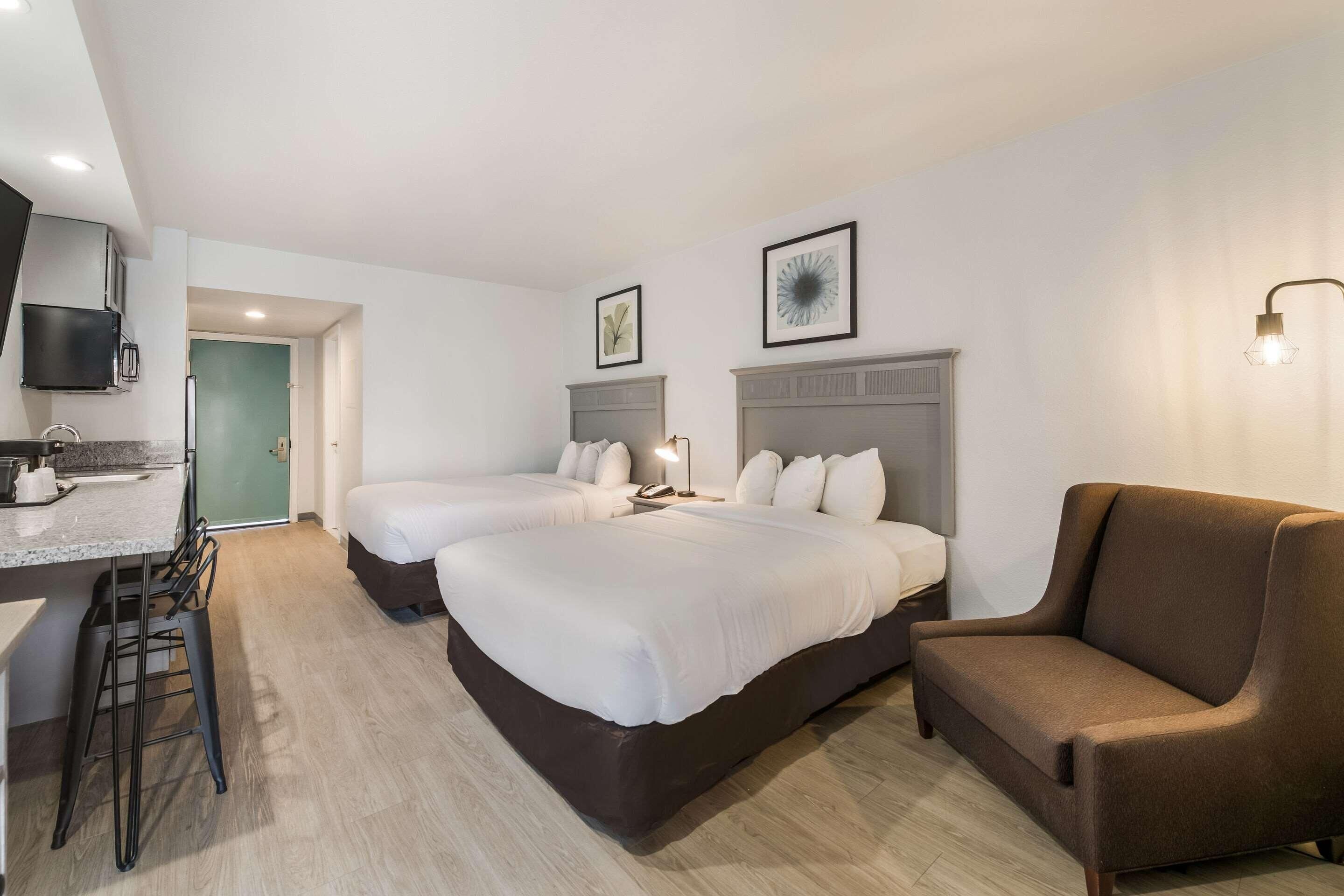 Et hotelværelse med to senge, en sofa, et skrivebord med stol og et fjernsyn ophængt på væggen.