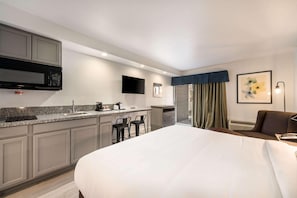 A hotel room with a kitchenette, a bed, a seating area, and a TV. - Suburban Williamsburg (Williamsburg)