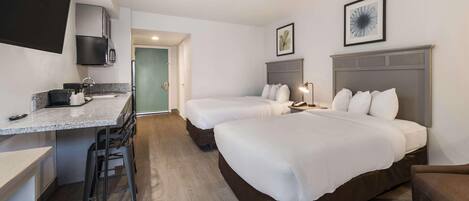 Hotellihuone, jossa on pieni keittiö, kaksi sänkyä, työpöytä ja tuoli.