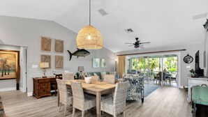 Amplia sala de estar con una mesa de comedor de madera, sillas de mimbre, una lámpara colgante grande de tejido y vistas al exterior.