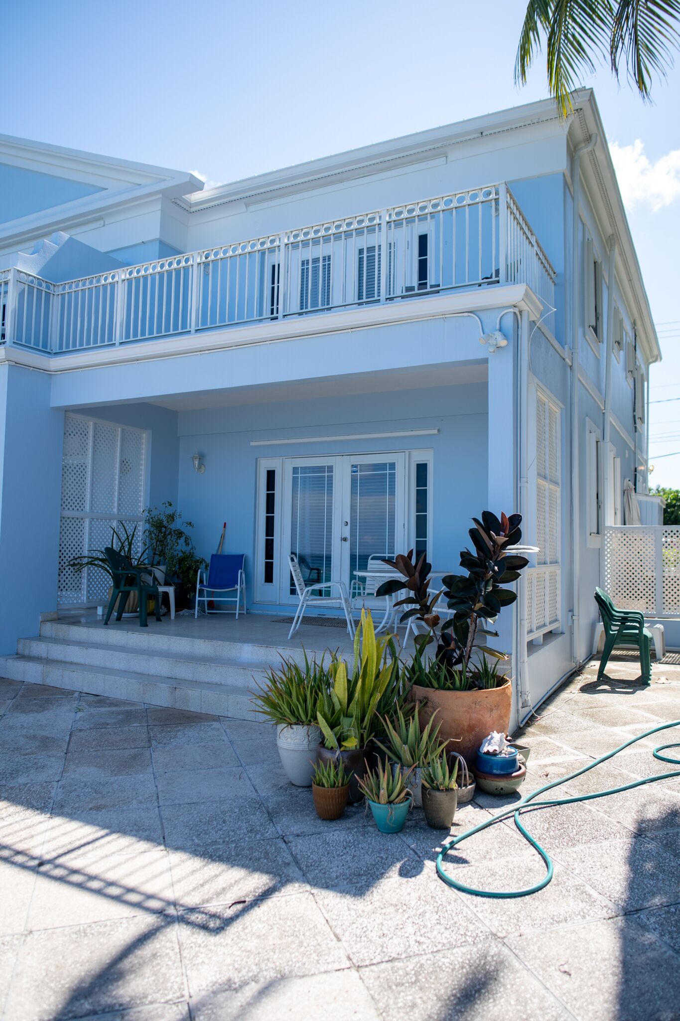Uma casa de dois andares com varanda, plantas em vasos e móveis de exterior.