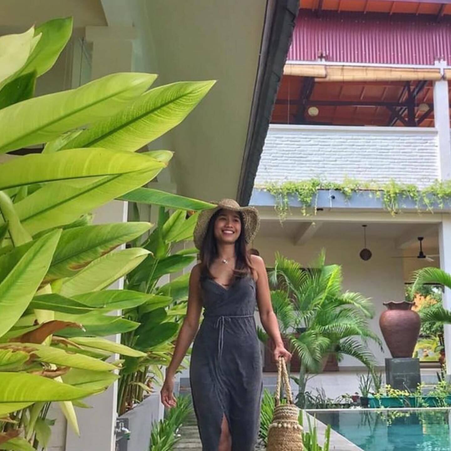 A person walking in a covered outdoor area with large green plants and a pool.