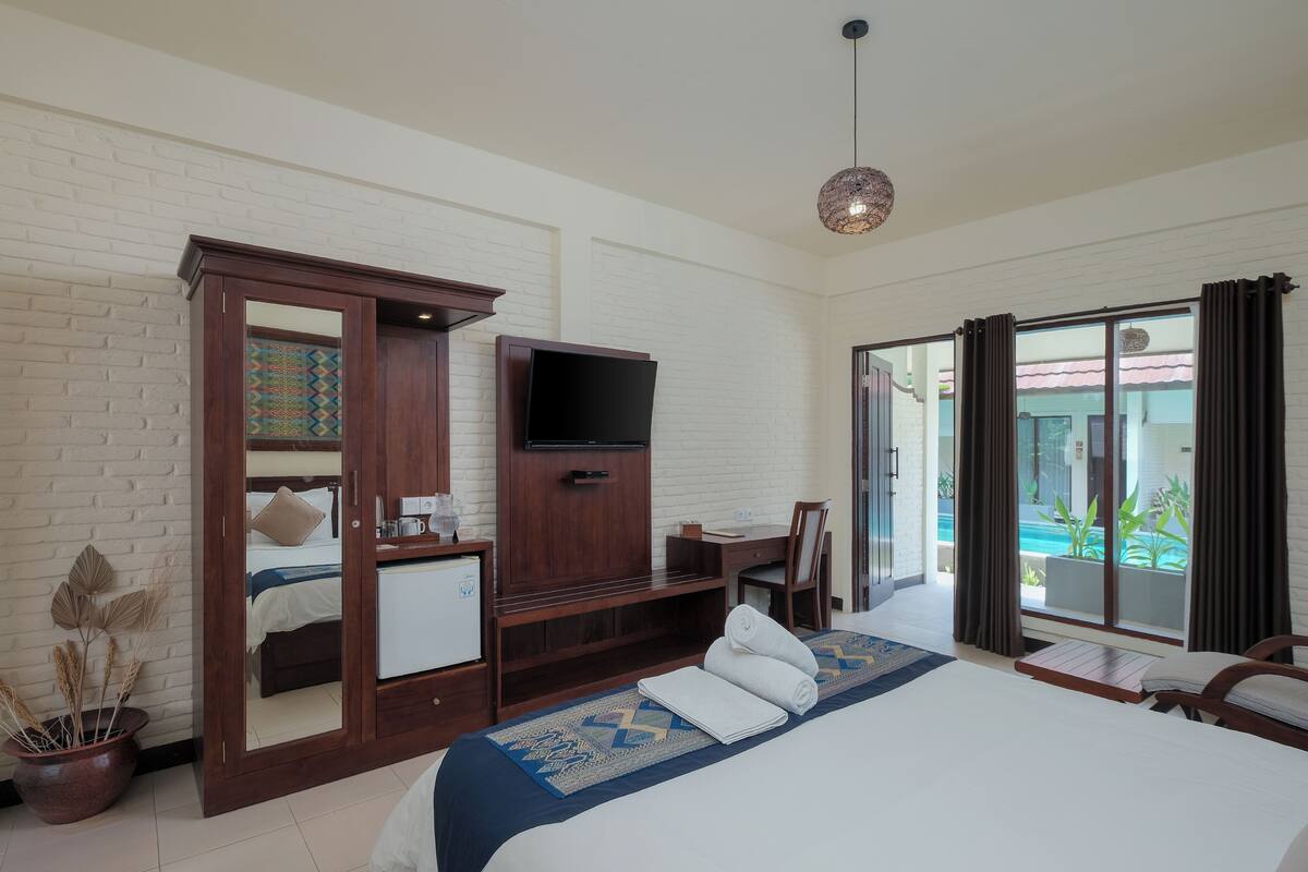 Habitación de hotel con cama, escritorio, televisor, armario y vista a la piscina.
