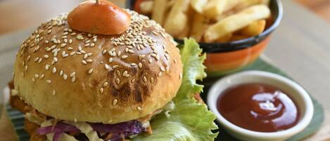 A burger with a sesame seed bun, a fried patty, lettuce, and a tomato on top, served with French fries and ketchup.