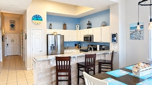 A modern kitchen with white cabinets, a stainless steel refrigerator, and a breakfast bar with two chairs.