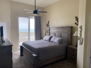 Ein Schlafzimmer mit einem Bett, einem Deckenventilator, einem Nachttisch, einer Kommode und Blick ins Freie.